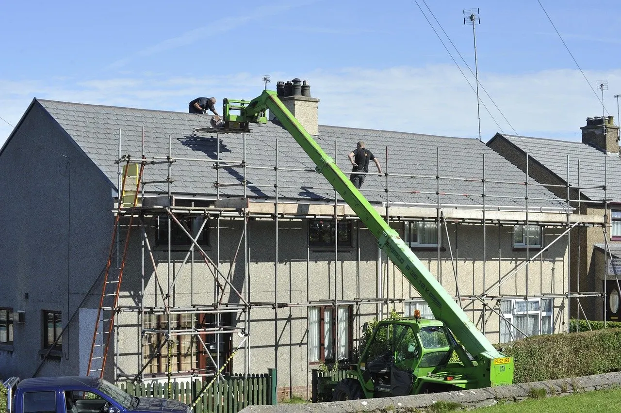 Zwei Arbeiter auf einem Dach eines Hauses mit Gerüst, daneben ein grüner Teleskoplader.