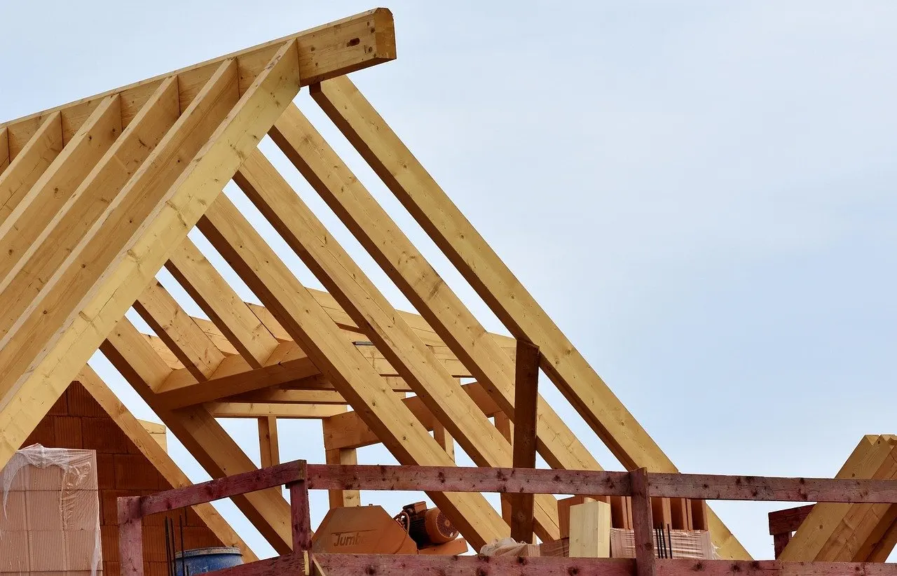 Holzdachkonstruktion mit Sparren und Pfetten auf einer Baustelle, im Hintergrund Mauerwerk und Schutzgeländer.