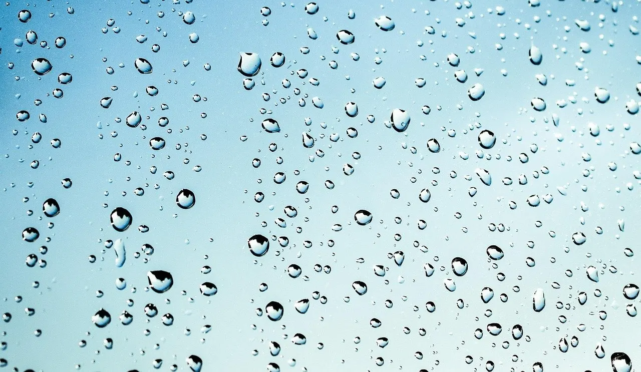 Viele Wassertropfen auf einer Glasscheibe vor blauem Himmelshintergrund.
